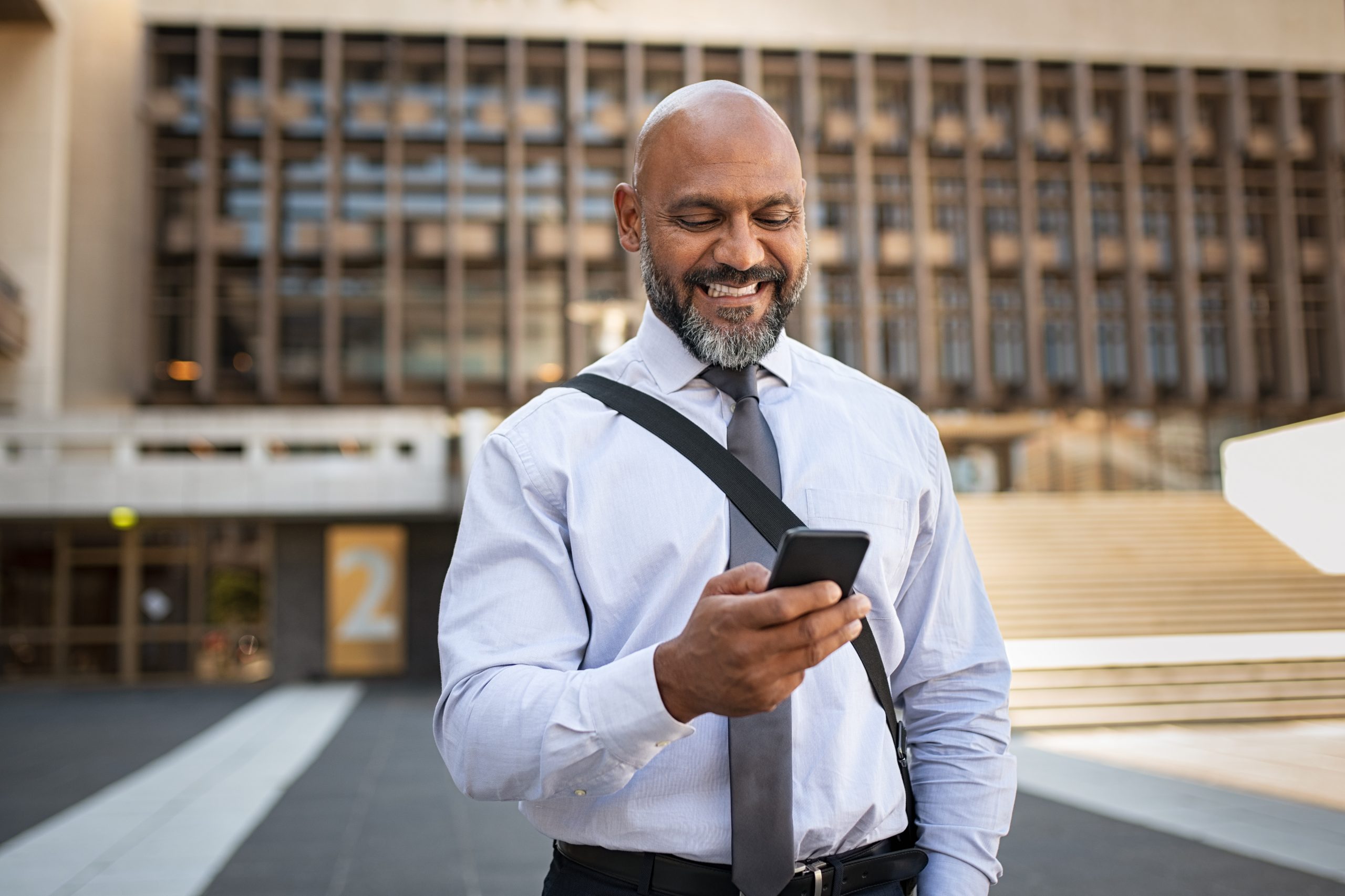 Happy formal businessman using phone on street